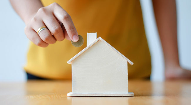 main glissant une pièce dans une tirelire en forme de maison