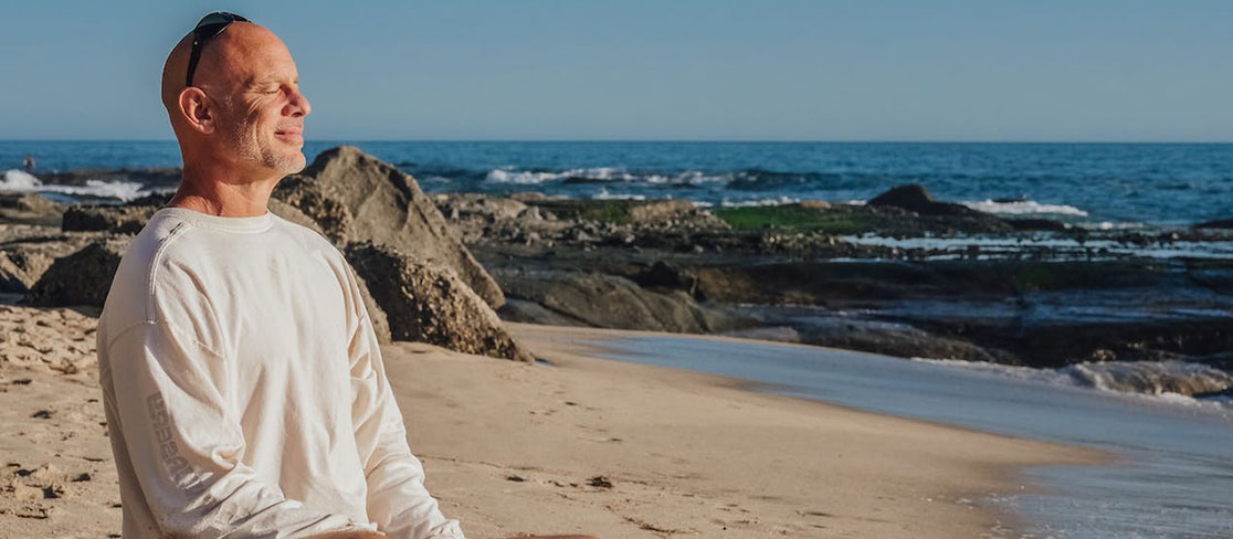 senior souriant sur une plage, en position de méditation